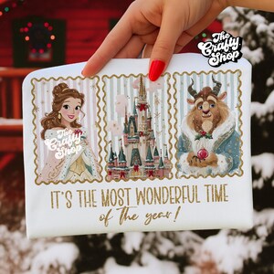 Puede incluir: Camiseta blanca con ilustraciones de Bella, la Bestia y un castillo de La Bella y la Bestia. El texto "IT'S THE MOST WONDERFUL TIME of the year!" est&aacute; en dorado. El logo The Crafty Shop es visible.