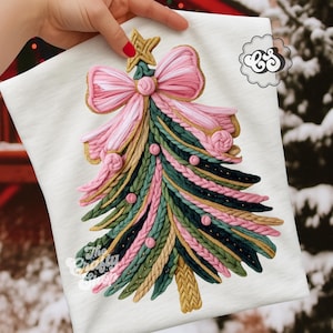 Pode incluir: Camiseta branca com um design detalhado de árvore de Natal. A árvore é feita com elementos texturizados rosa, verde e dourado, incluindo um grande laço rosa e uma estrela dourada. O texto "The Crafty Siren" está impresso na parte inferior.