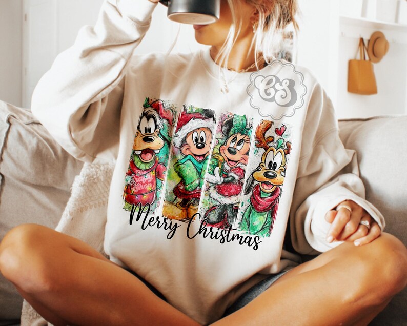 Puede incluir: Sudadera color crema con un dise&ntilde;o festivo con personajes de dibujos animados. El dise&ntilde;o incluye a Goofy, Mickey Mouse, Minnie Mouse y Pluto, cada uno con atuendos navide&ntilde;os. Las palabras "Merry Christmas" est&aacute;n escritas en una fuente cursiva.