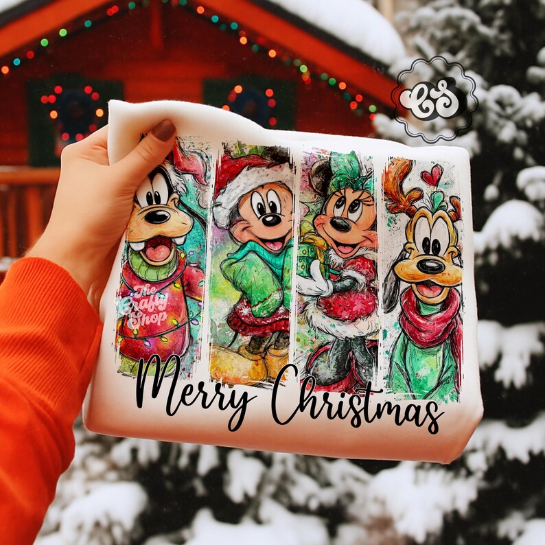 Puede incluir: Bolso tote blanco con una ilustraci&oacute;n colorida de los personajes de Disney Goofy, Mickey Mouse, Minnie Mouse y Pluto con atuendos navide&ntilde;os. Las palabras "Merry Christmas" est&aacute;n escritas en una fuente cursiva debajo de los personajes. Tambi&eacute;n se ven las palabras "The Crafty Shop".