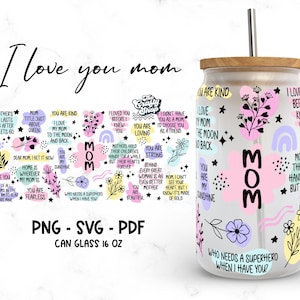 Pode incluir: Um copo de vidro transparente de 473 ml com tampa de madeira e um canudo. O copo é decorado com formas abstratas coloridas, flores e texto que diz "Amo minha mãe até a lua e de volta" e "Quem precisa de um super-herói quando eu te tenho?"