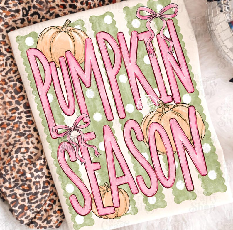 May include: A white t-shirt featuring a graphic print with the text PUMPKIN SEASON in large pink letters. The design includes three light orange pumpkins, two pink bows, and a background of vertical sage green stripes with white polka dots.