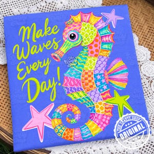 Pode incluir: Uma placa quadrada azul com um cavalo-marinho colorido com um padrão de retalhos em amarelo, rosa, laranja e verde. O texto "Make Waves Every Day!" está impresso em amarelo brilhante. Uma estrela rosa claro e uma verde-limão são visíveis.
