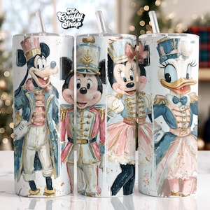 May include: Four stainless steel tumblers featuring Disney characters in Nutcracker-themed outfits. Mickey Mouse, Minnie Mouse, and Daisy Duck are depicted in colorful, detailed illustrations. Each tumbler has a straw and the logo "The Crafty Shop".