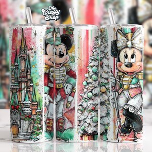 Könnte beinhalten: Drei Edelstahlbecher mit Strohhalmen zeigen Aquarelldesigns. Ein Becher zeigt ein Schloss, ein anderer Micky Maus in einer Nussknacker-Uniform und der dritte einen Weihnachtsbaum und Minnie Maus in einer Nussknacker-Uniform. Das Logo The Crafty Shop befindet sich oben.