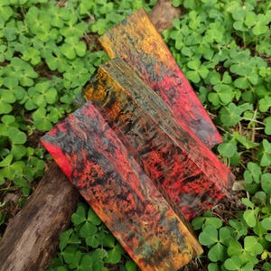 May include: Three rectangular blocks of stabilized wood featuring a vibrant, swirling pattern of red, black, and yellow tones. The wood grain displays a complex, marbled texture with deep color saturation throughout each individual piece.