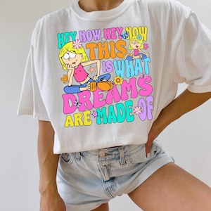 Op de afbeelding: Wit T-shirt met een kleurrijke grafische print met twee cartoonmeisjes en de tekst "Hey Now Hey Now This Is What Dreams Are Made Of".