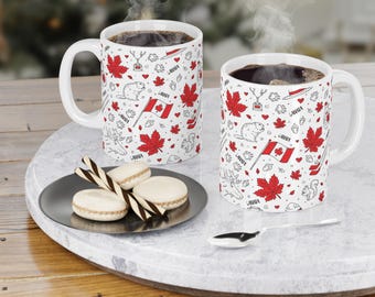May include: Two white ceramic mugs with a red, white and black design featuring Canadian symbols such as maple leaves, beavers, and the Canadian flag. The mugs are filled with coffee and are sitting on a round, white surface.