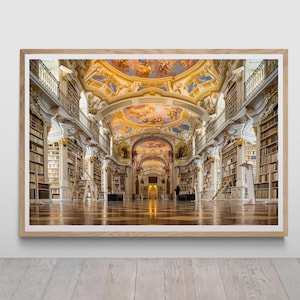 May include: A framed print of a grand library interior. The room features high ceilings with ornate painted details, rows of bookshelves, and a polished wooden floor. The color palette includes gold, white, and warm wood tones, creating a sense of historical elegance.