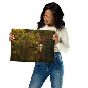 May include: A photograph of a lake with a small cabin on the shore. The trees surrounding the lake are in autumn colors, with shades of red, orange, yellow, and green. The water is still and reflects the colors of the trees.