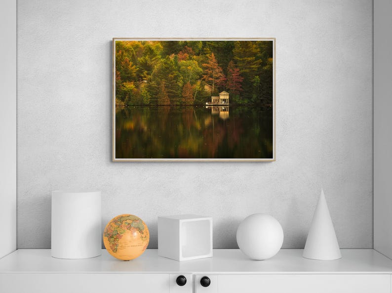 May include: A photograph of a small wooden cabin on a lake surrounded by trees with fall foliage. The cabin is reflected in the still water.