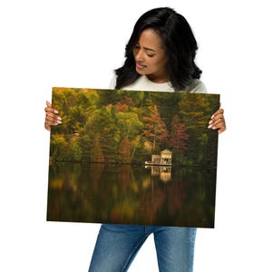May include: A photograph of a lake with a small cabin on the shore. The lake is surrounded by trees with fall foliage in shades of red, orange, yellow, and green. The water is calm and reflects the colors of the trees.