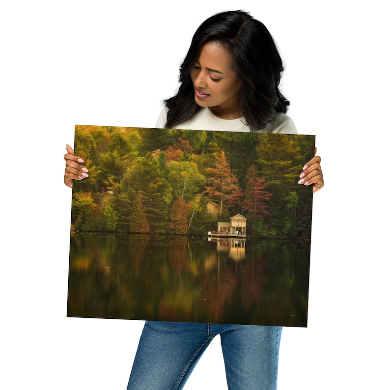 May include: A photograph of a lake with a small cabin on the shore. The lake is surrounded by trees with fall foliage in shades of red, orange, yellow, and green. The water is calm and reflects the colors of the trees.