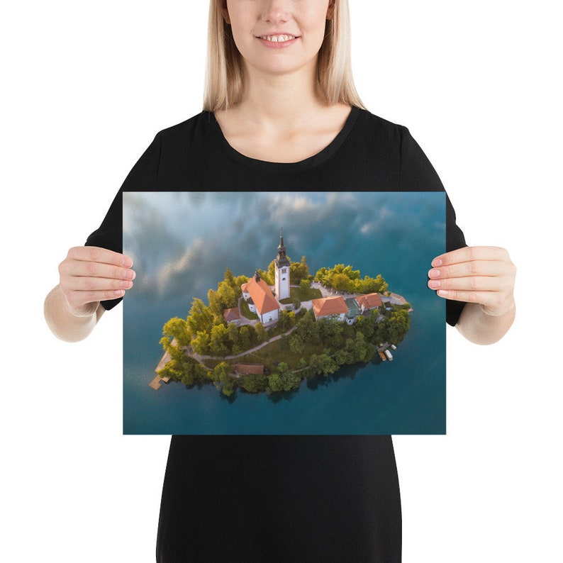 Puede incluir: Un p&oacute;ster con una vista a&eacute;rea de una isla con una iglesia y edificios rodeados de agua. La iglesia tiene un alto campanario blanco y un tejado rojo. La isla est&aacute; cubierta de &aacute;rboles verdes y rodeada de agua azul.