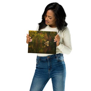 May include: A photograph of a lake with trees in the background and a small cabin on the water. The water is reflecting the colors of the trees and the sky. The photo is printed on a high-quality canvas.