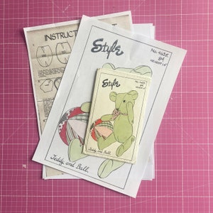 May include: A vintage sewing pattern for a teddy bear and ball. The pattern is printed on white paper with a green teddy bear and a multi-colored ball. The pattern is titled "Teddy and Ball" and includes instructions for sewing the toy. The pattern number is 4635 and the height is 14 inches.