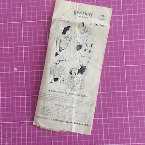Op de afbeelding: Vintage Bestway patroon voor een blouse met vijf modellen. Het patroon bevat illustraties van de blouse-ontwerpen en materiaaleisen voor verschillende borstmaten. Het patroon is gedrukt op verouderd papier en ligt op een roze snijmat.