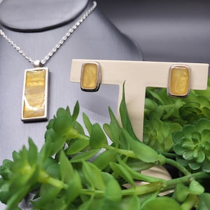 May include: A set of yellow resin jewelry featuring a pendant necklace and matching earrings. The pendant and earrings are rectangular in shape with a silver frame.