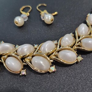 May include: A gold necklace with white oval-shaped pearls and clear rhinestones. Matching earrings with white pearls and clear rhinestones.