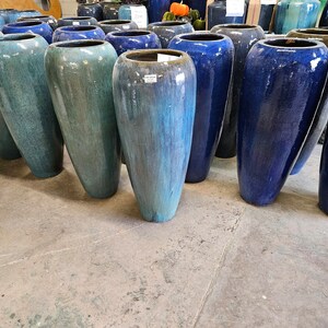 May include: A row of tall, blue and green ceramic planters. The planters are all different shades of blue and green, and they are all very tall and slender.