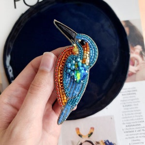 Pu&ograve; includere: Un broche a forma di uccello realizzato con perline di colore blu, arancione e giallo. L'uccello ha un becco lungo e sottile e un corpo piccolo e rotondo. Il broche &egrave; fatto di piccole perline colorate cucite insieme per creare un design dettagliato. Il broche &egrave; un gioiello bellissimo e unico che sarebbe un ottimo regalo per qualsiasi amante degli uccelli.