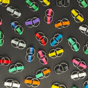 May include: A collection of colourful interlocking metal rings. The rings are made of silver metal and are connected by a variety of coloured plastic pieces. The rings are arranged in a random pattern on a black surface.