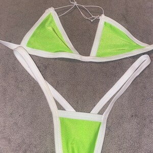 May include: A lime green bikini with white trim. The top is a triangle style with adjustable straps. The bottom is a cheeky style with a high leg cut.