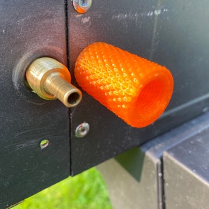 Puede incluir: Primer plano de una tapa de v&aacute;lvula de pl&aacute;stico naranja con una superficie texturizada. La tapa est&aacute; unida a una v&aacute;lvula de metal.