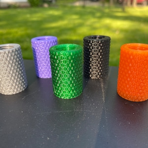 Puede incluir: Cinco objetos cil&iacute;ndricos de diferentes colores con una superficie texturizada. Los colores son gris, morado, verde, negro y naranja.