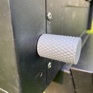 Puede incluir: Primer plano de una perilla blanca texturizada sobre una superficie negra. La perilla tiene un patr&oacute;n de diamante y se utiliza para controlar una parrilla de gas.