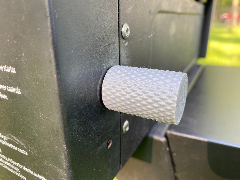 Puede incluir: Primer plano de una perilla blanca texturizada sobre una superficie negra. La perilla tiene un patr&oacute;n de diamante y se utiliza para controlar una parrilla de gas.