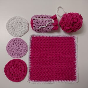 May include: Set of crocheted items in pink and white, including a washcloth, a pouf, a small bag, and three round scrubbers.