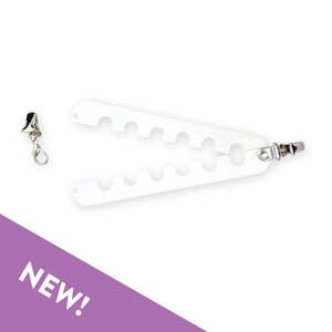 May include: A white plastic hanger with a scalloped edge design featuring six rounded notches along each side. The hanger is attached to a silver-toned metal clip on one end, and a separate silver-toned metal lobster clasp is positioned to the left.