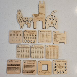 May include: A collection of light-colored wooden knitting tools and reference guides, including llama-shaped needle gauges, charts for sock and hat sizes, a Kitchener stitch guide, a 1-inch gauge ruler, and a color palette tool with circular cutouts.