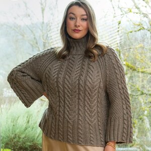 May include: A taupe-colored knit sweater featuring a high turtleneck, long sleeves with wide cuffs, and a prominent vertical cable knit pattern across the front. The garment includes the text Berroco Mirelle 462 at the top of the image.