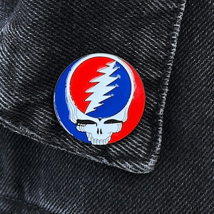 May include: A red, white, and blue enamel pin featuring the Grateful Dead's iconic Steal Your Face logo.