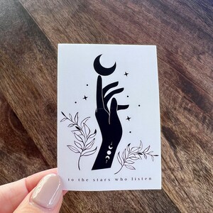 K&ouml;nnte beinhalten: Eine Schwarzwei&szlig;illustration einer Hand, die nach einem Halbmond mit Sternen und Bl&auml;ttern darum herum greift. Der Text "to the stars who listen" befindet sich unter dem Bild.