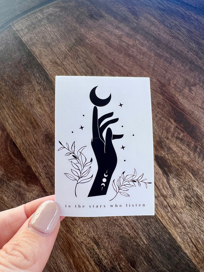 K&ouml;nnte beinhalten: Eine Schwarzwei&szlig;illustration einer Hand, die nach einem Halbmond mit Sternen und Bl&auml;ttern darum herum greift. Der Text "to the stars who listen" befindet sich unter dem Bild.