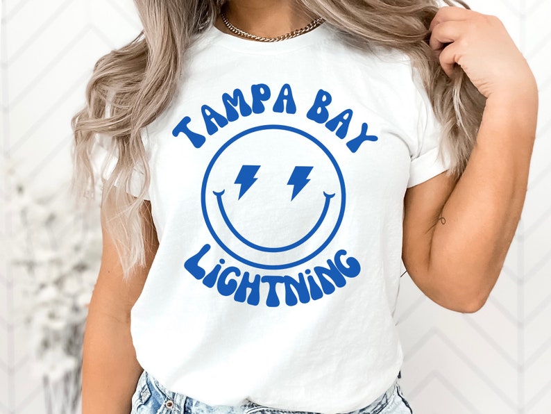 May include: White t-shirt with a blue smiley face graphic and the text "Tampa Bay Lightning" in a retro font.
