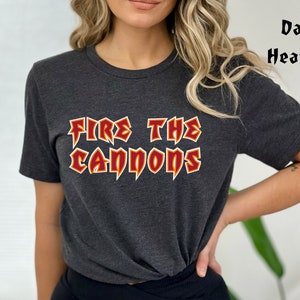 Puede incluir: Camiseta gris oscuro con el texto "FIRE THE CANNONS" en un diseño audaz en rojo y amarillo. La camiseta es de cuello redondo y manga corta.