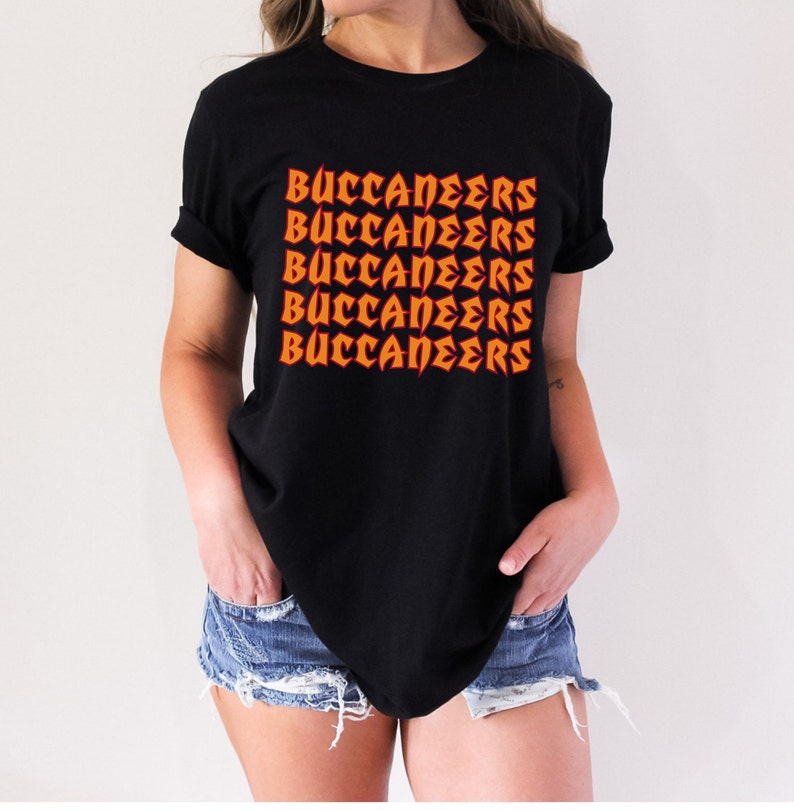 May include: Black t-shirt with the word "BUCCANEERS" printed in orange, repeated five times. The text has a bold, stylized font. The shirt is a crew neck style.