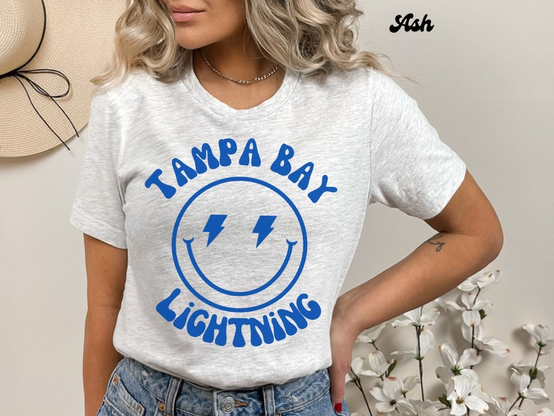 May include: A gray t-shirt with a blue smiley face graphic and the text "Tampa Bay Lightning" in a retro font.
