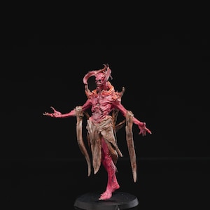 Op de afbeelding: Gedetailleerd beeldje van een rode demon met hoorns, uitgestrekte armen en een versleten doek om zijn middel. De figuur staat op een zwarte basis tegen een donkere achtergrond, met ingewikkelde details en texturen.
