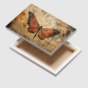 May include: A canvas print featuring a butterfly with orange and black wings against a textured, sepia-toned background. The artwork is mounted on a white frame, showcasing the butterfly's intricate details and the canvas's texture.