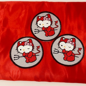May include: Three iron-on patches featuring a red cartoon character with a devil tail and horns. The character has a pink bow and is holding a pitchfork. The patches are on a red fabric background.