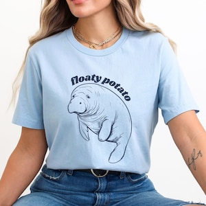 May include: A light blue t-shirt with a graphic of a manatee and the text "floaty potato" in a retro font.