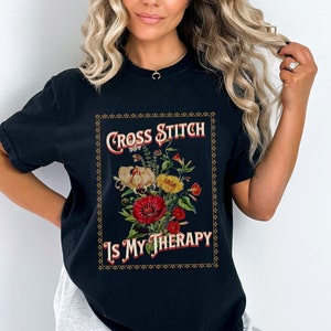 May include: Black t-shirt with a vintage-style graphic that says "Cross Stitch Is My Therapy" with a floral design.