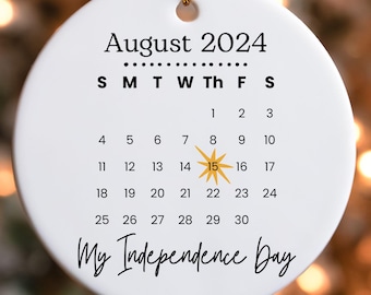 May include: White ceramic ornament with a calendar for August 2024. The 15th is highlighted with a yellow star and the text "My Independence Day" is written below the calendar.