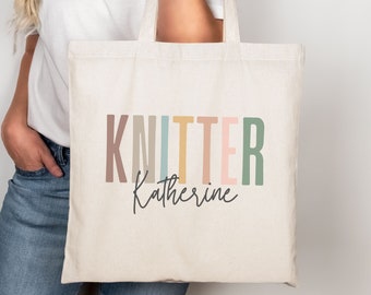 May include: A white canvas tote bag with the text "KNITTER Katherine" in colorful letters. The letters are in shades of brown, blue, yellow, pink, and green.