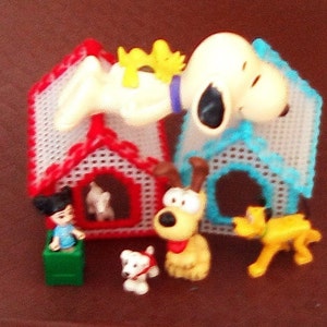 May include: A collection of cartoon character figurines and dog houses. The dog houses are red and blue with white mesh. The figurines include a girl, a white dog with a red scarf, a yellow dog with a red collar, and a yellow dog.